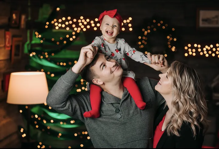 A father carrying a laughing child on his shoulders, the mother smiling beside them