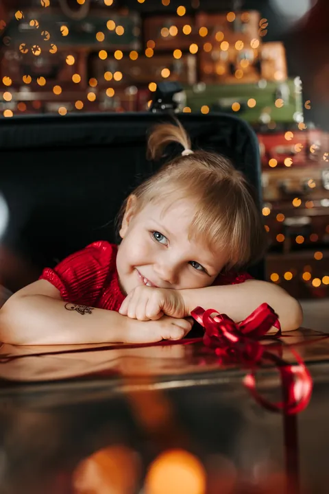 A smiling girl resting her head on her hands with a red gift ribbon in front