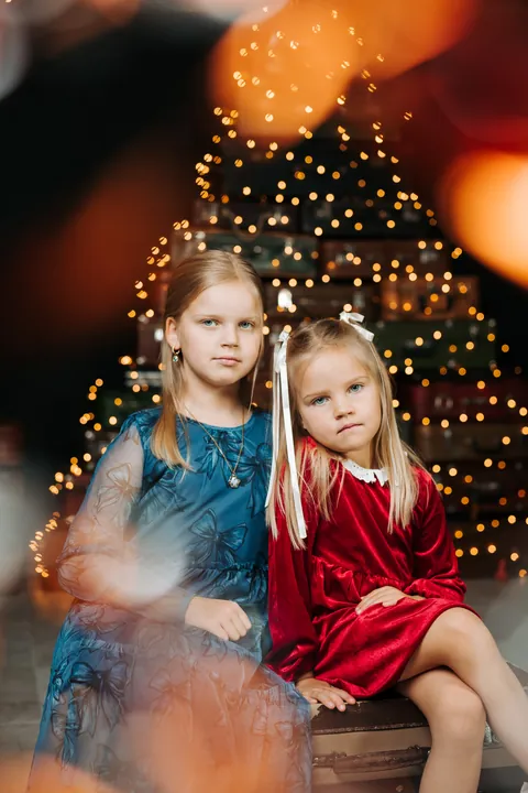 Two sisters sitting in front of a sparkling Christmas tree