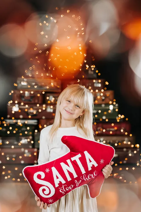 A girl holding a SANTA pillow in front of the suitcase Christmas tree in Merle's studio