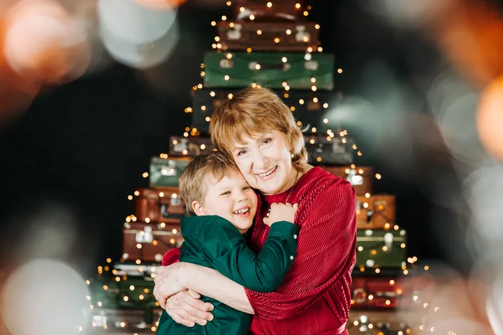 A grandmother and grandchild hugging in front of a suitcase Christmas tree