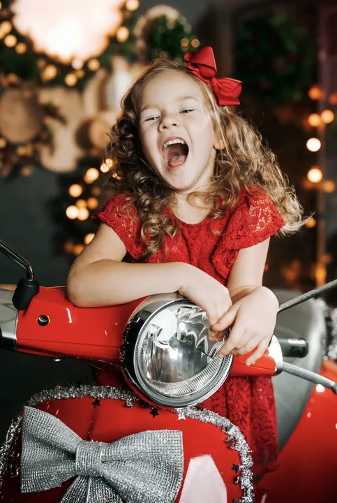 A laughing girl in a red dress by a red scooter