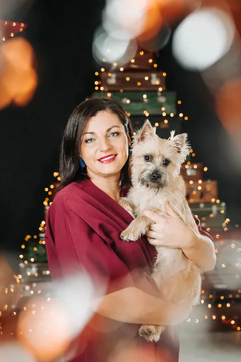 A woman holding a terrier in front of a Christmas tree