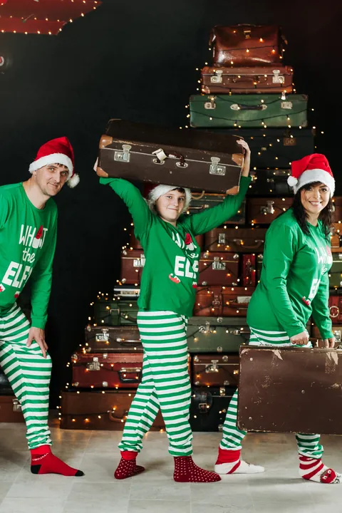 A family in green Christmas outfits in front of a Christmas tree made of suitcases in Merle's studio in 2025