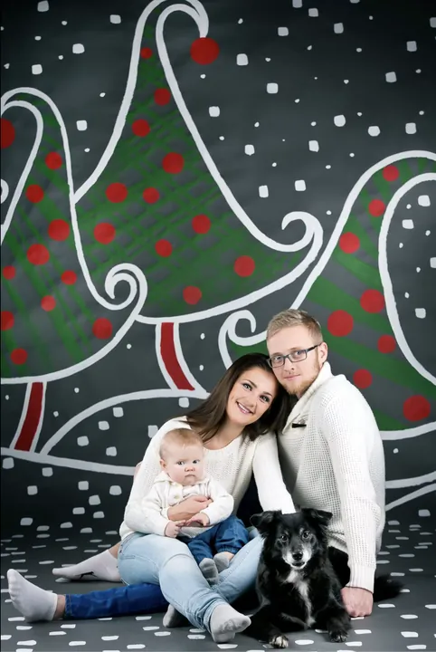 A family with a baby and a dog against painted Christmas trees
