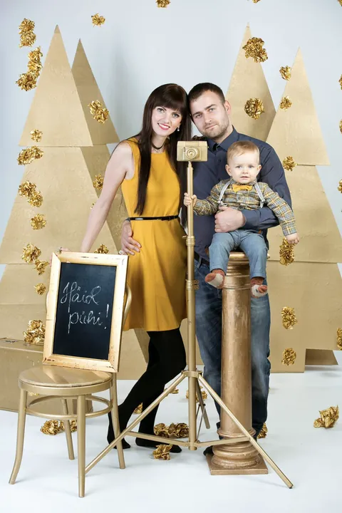 A family with a toddler in front of golden paper Christmas trees