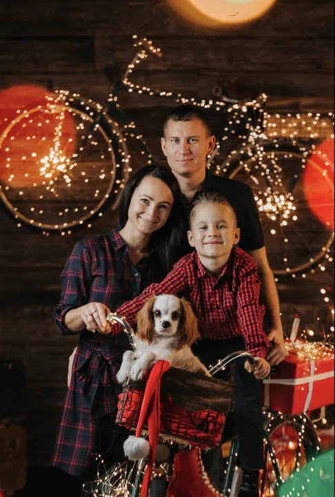 A family with a dog and a red bicycle in front of Christmas lights