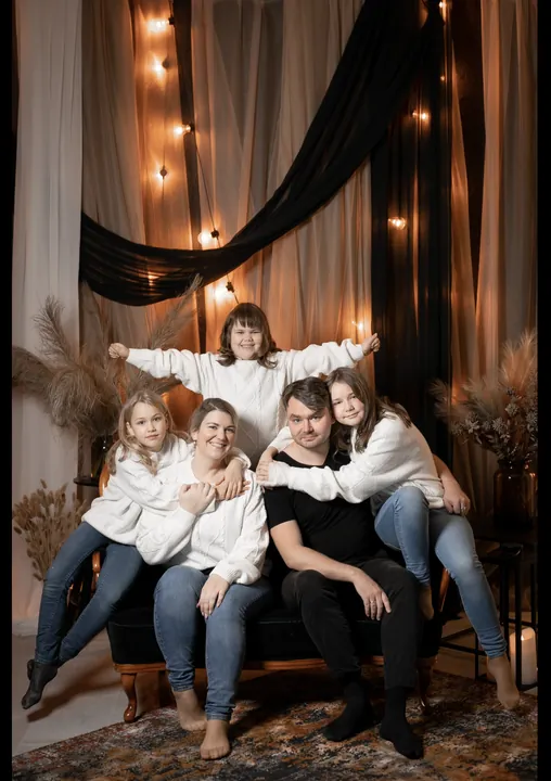 A big family in light clothes on a dark sofa in front of curtains