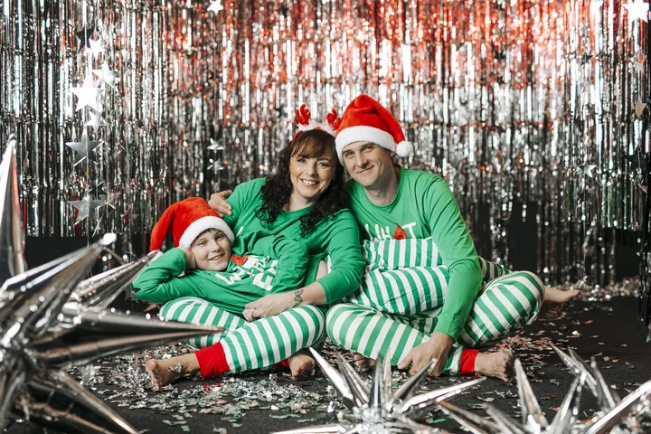 A family in elf hats in front of a sparkling silver backdrop