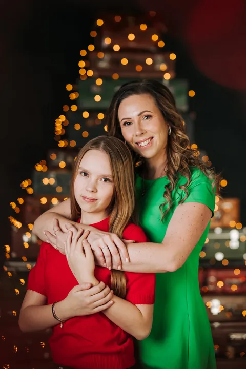 A mother and daughter hugging in front of a Christmas tree made of suitcases